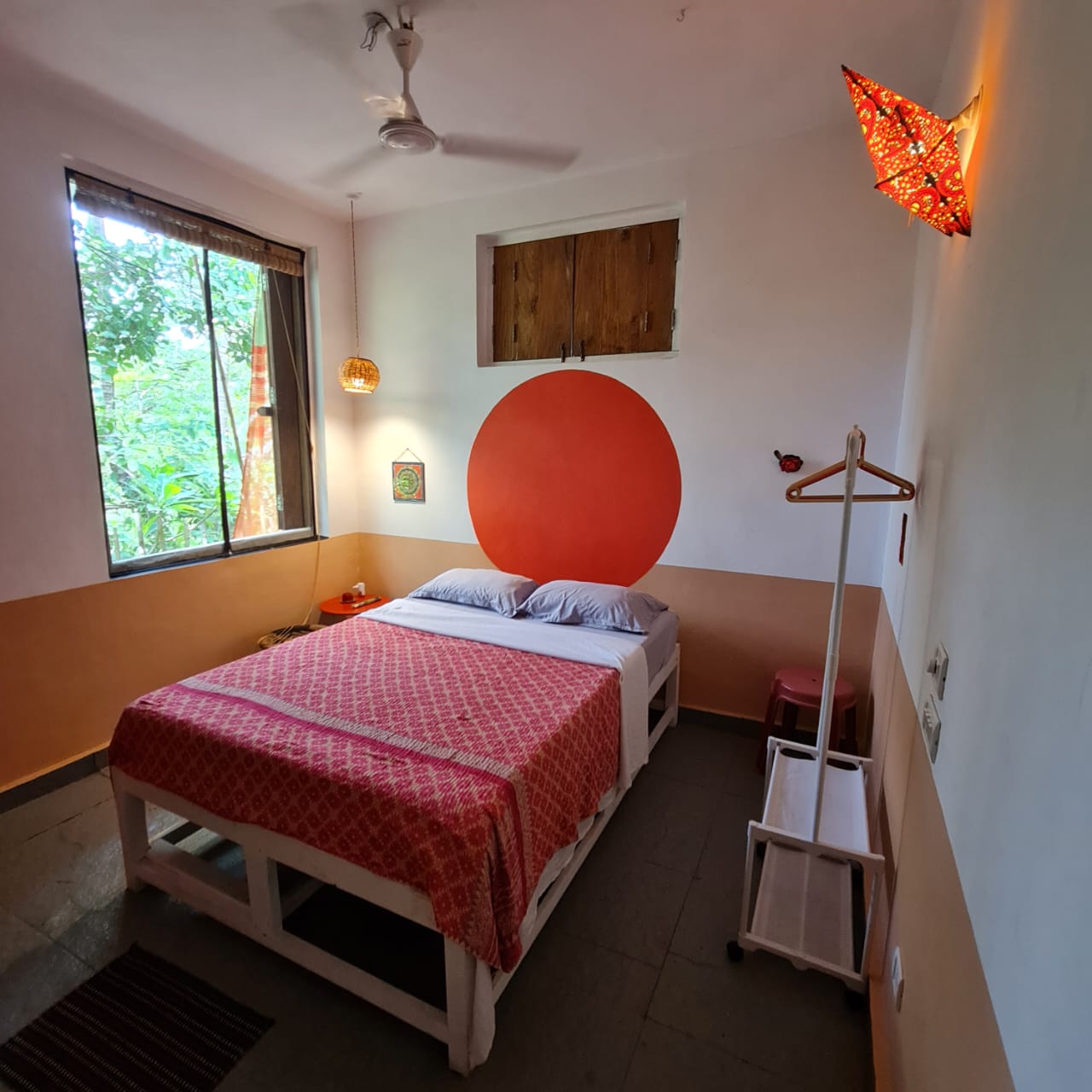 Prithvi room with a red bedspread, earth-toned walls and leafy window views