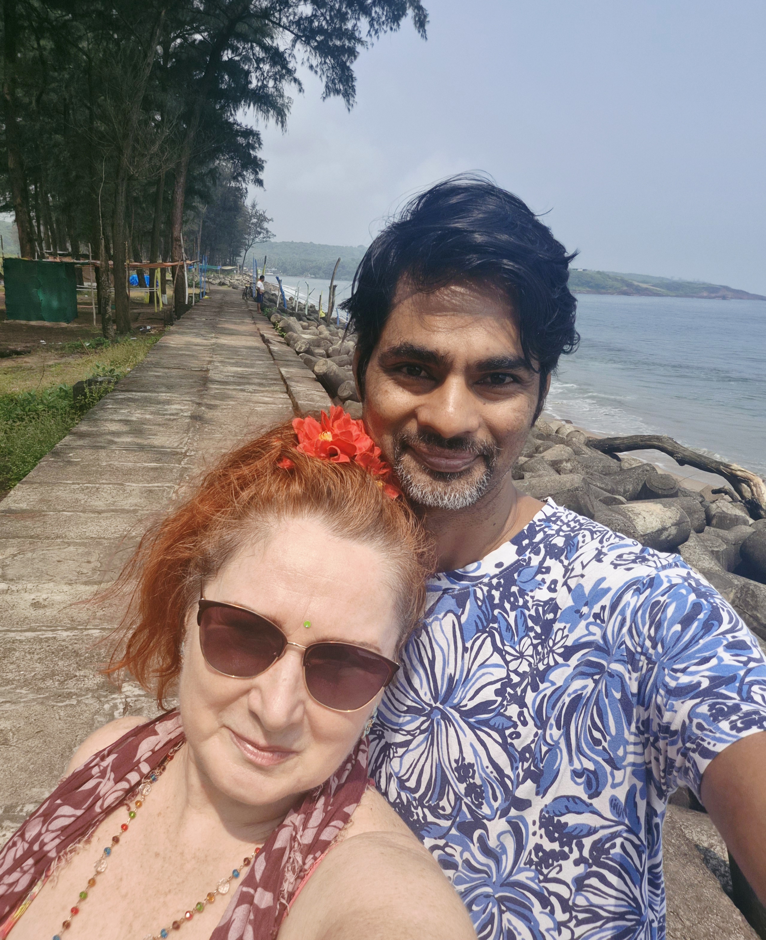 Two people beside the sea and tree-lined coastal walkway